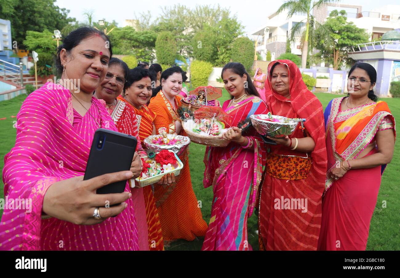 Beawar, Rajasthan, India, August 2, 2021: Hindu women wearing colorful lahariya saree, take a selfie with the idols of Laddu Gopal (Lord Krishna) as they celebrate the holy month of Sawan (Shravan) in Beawar. Photo: Sumit Saraswat Stock Photo