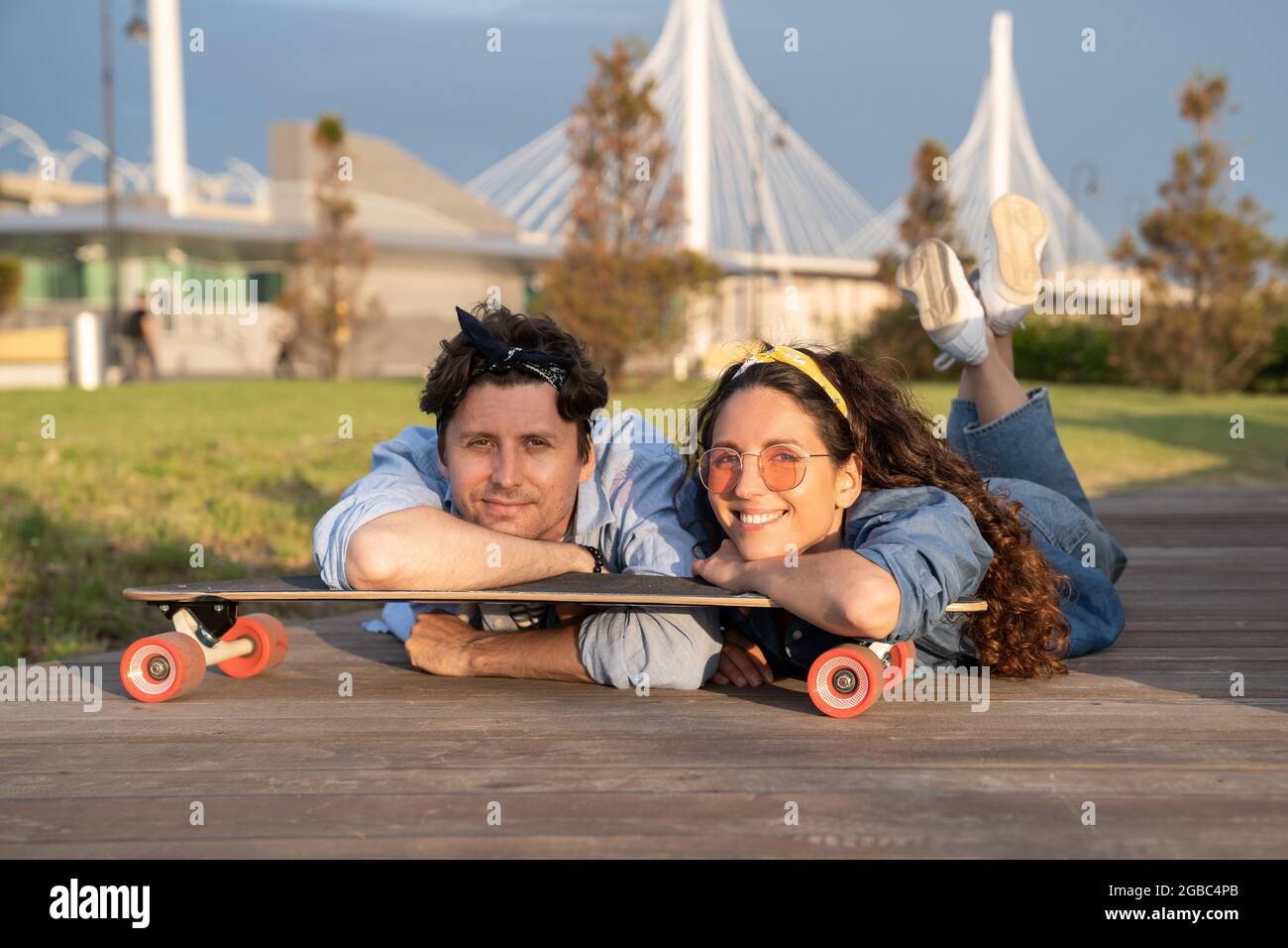 Young smiling couple chilling on longboard in city park at summer sunset. Urban lifestyle concept Stock Photo