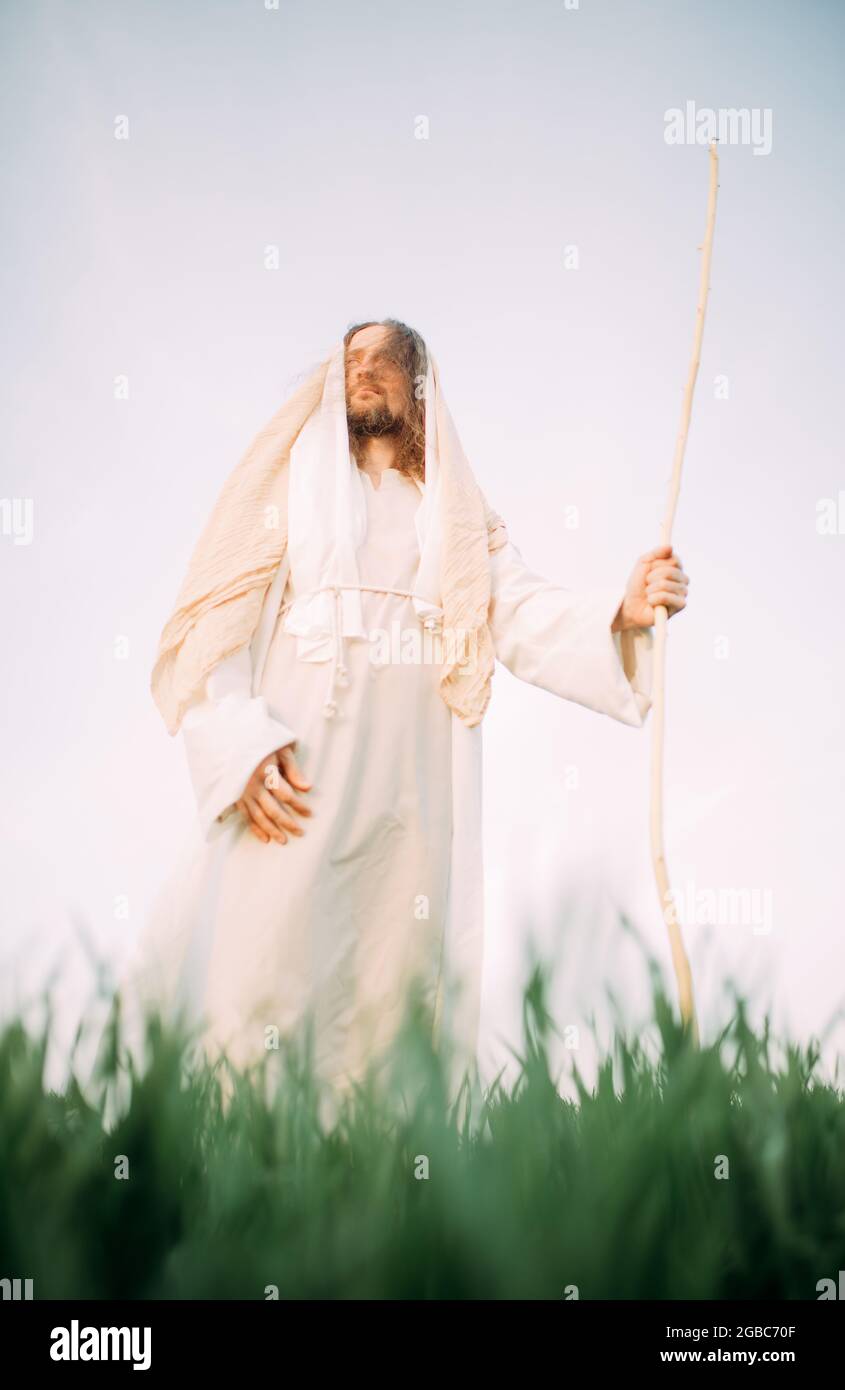 Jesus Christ with wooden staff stands in meadow clothed in his