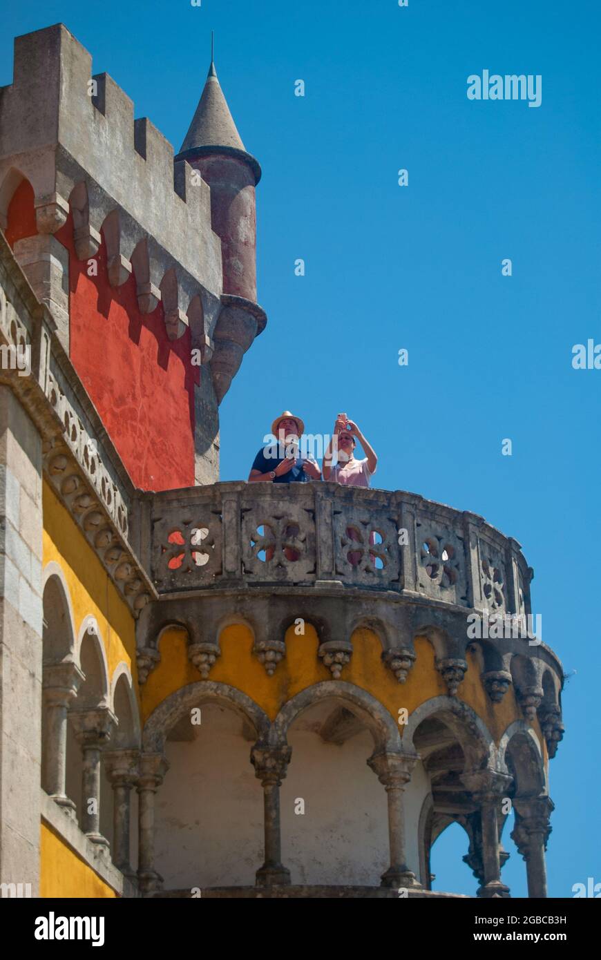 Beautiful yellow and red Pena Palace with tedious ornaments, a man and a woman are taking pictures from the balcony Stock Photo