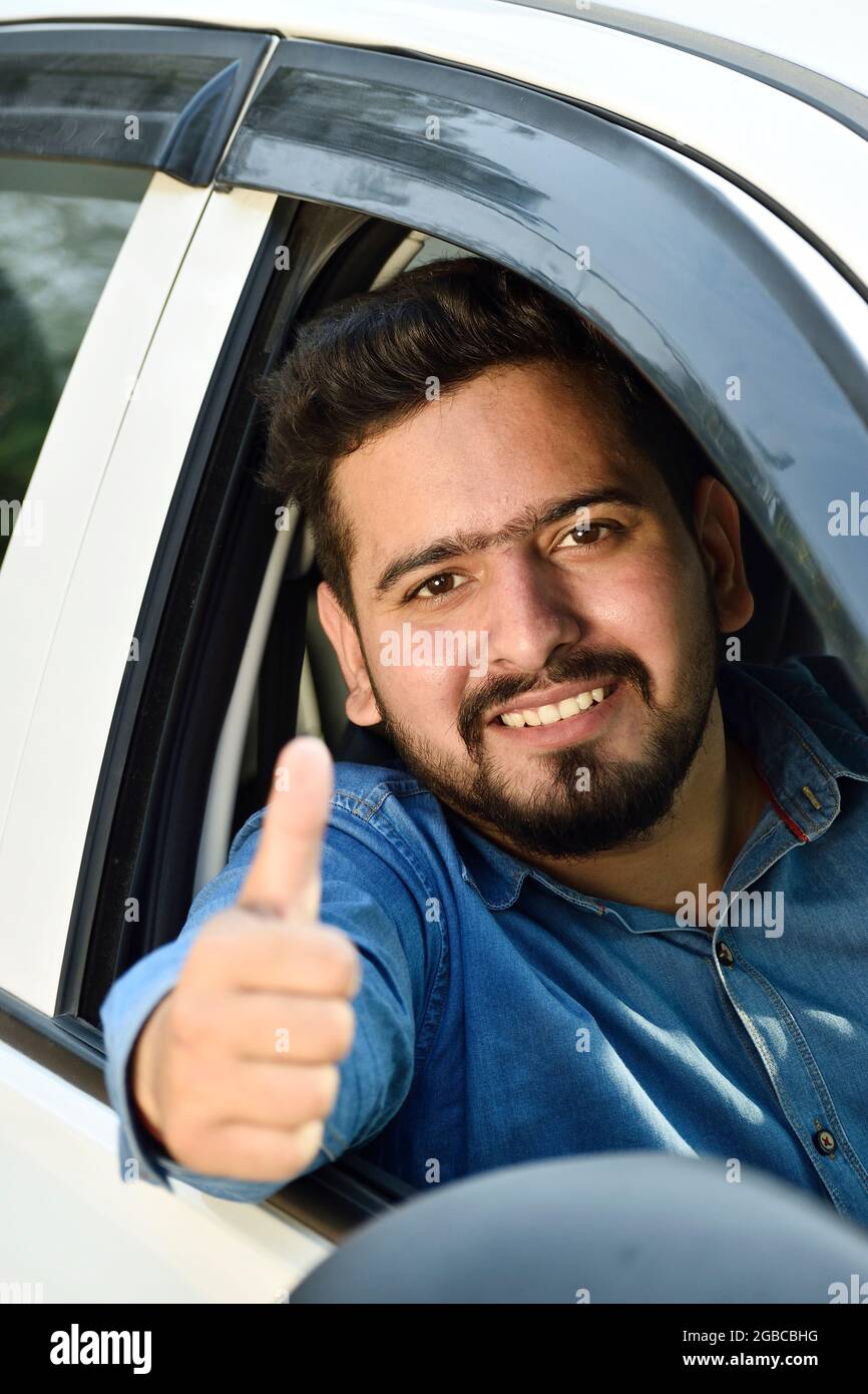 young Indian driver showing thumbs up sitting in car Stock Photo