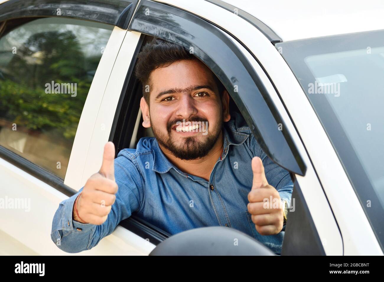 young Indian man showing thumb's up from car, Stock Photo