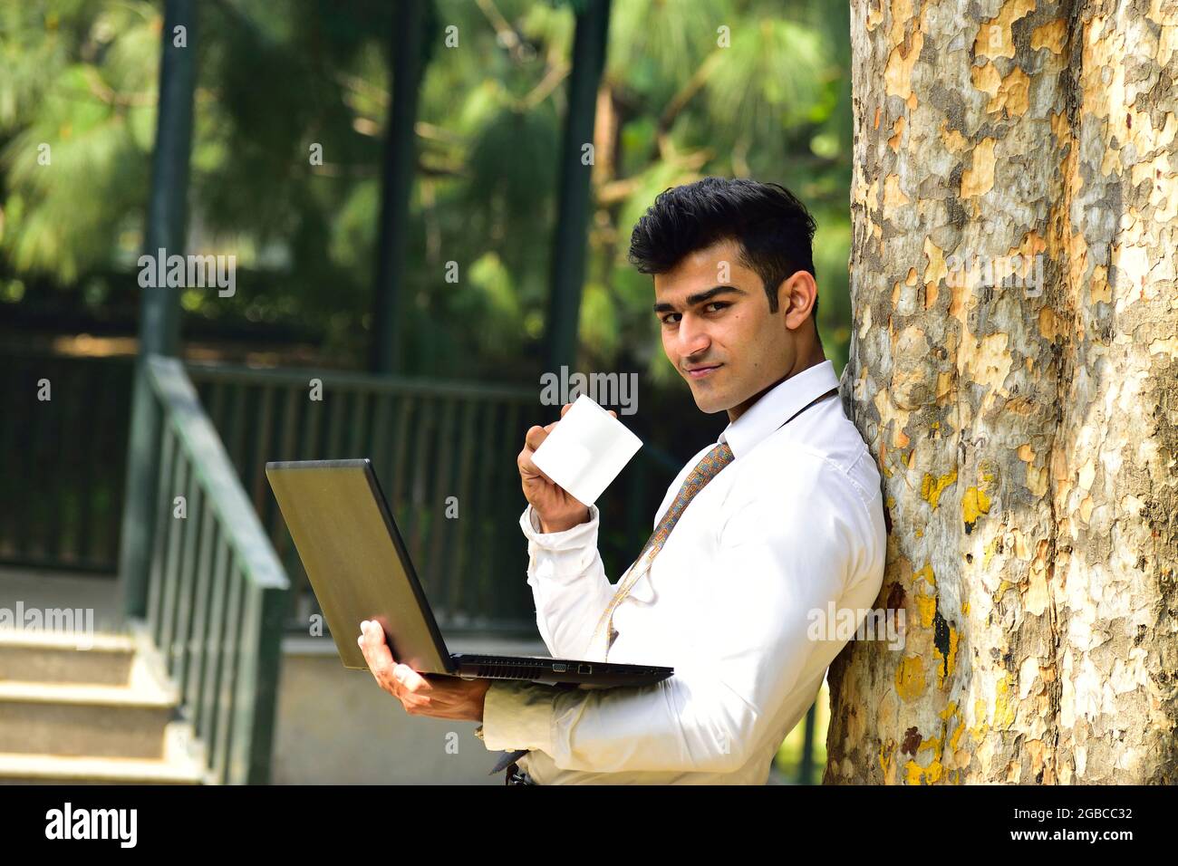 Young Indian Businessman Working Outdoor On Laptop and Drinking Coffee Stock Photo