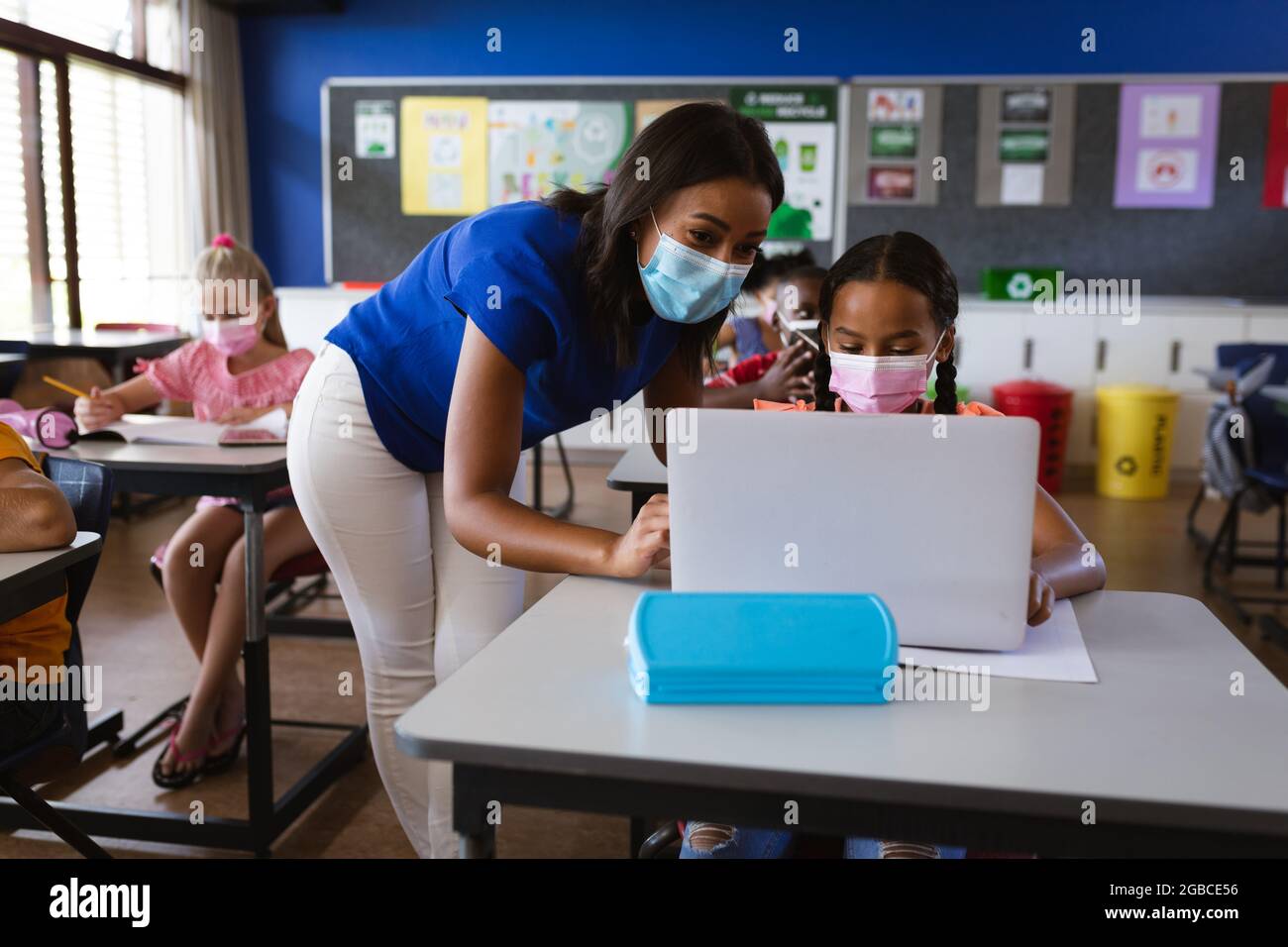 African american female teacher wearing face mask teaching a girl to ...