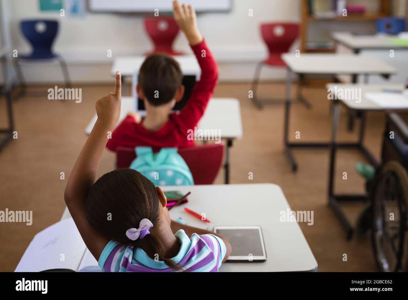 Rear view of african american girl raising her hand while sitting on ...