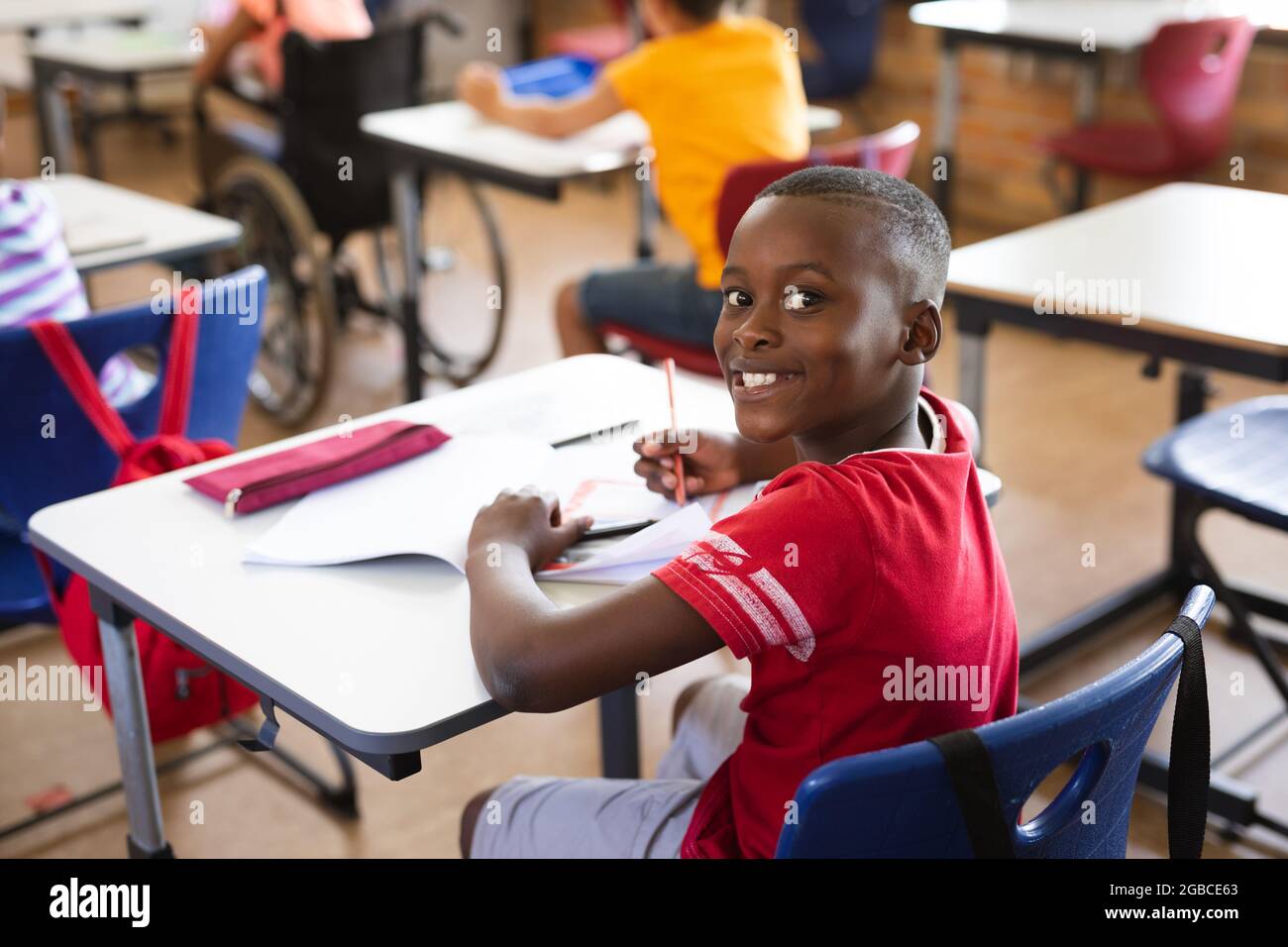 Portrait of african american boy smiling while sitting on his desk in ...