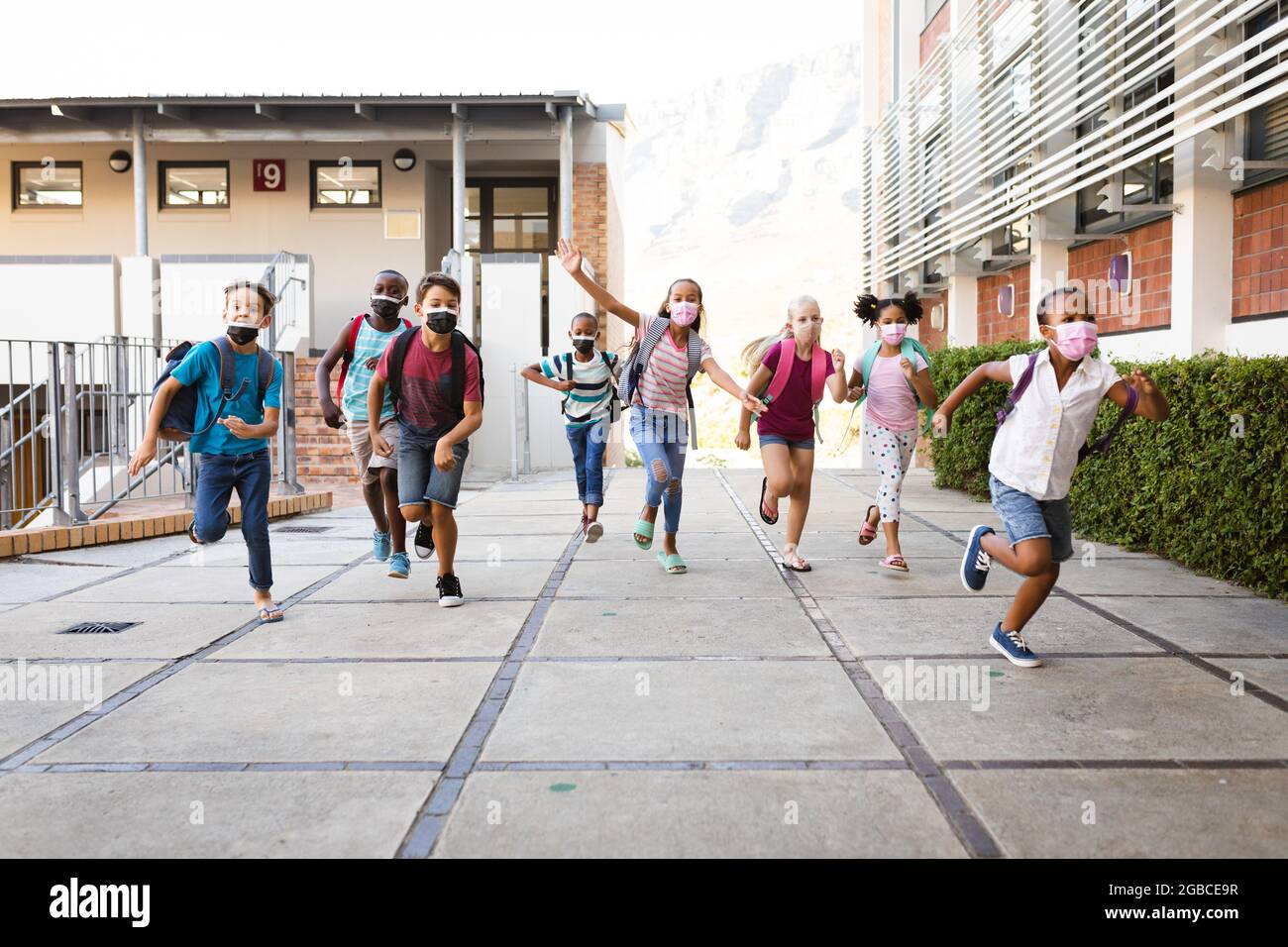 Group of diverse students wearing face masks running at elementary school Stock Photo