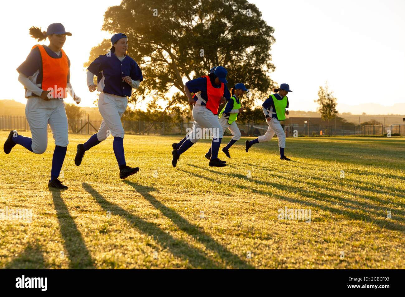 Diverse group of female baseball players warming up on field at sunrise, running Stock Photo