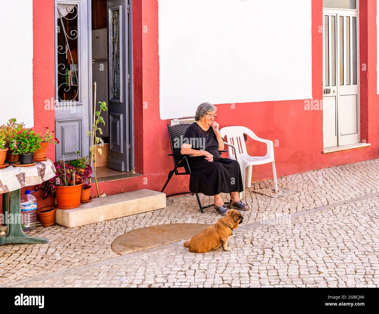 Old woman with her dog sitting outside her house on a warm day. Fuseta Algarve Portugal Stock Photo
