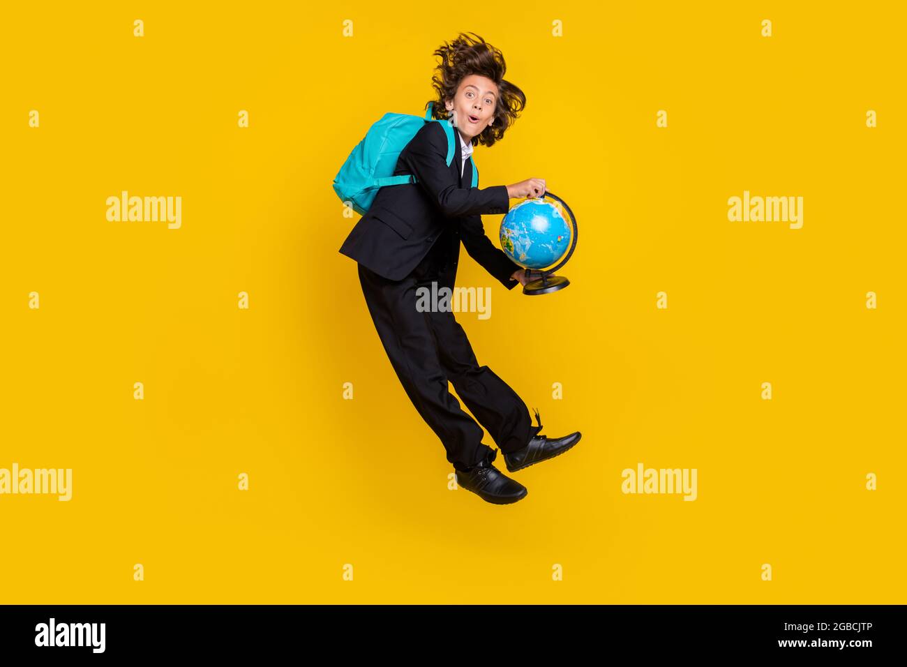 Photo of shocked surprised little boy jump hold globe wear rucksack black uniform isolated yellow color background Stock Photo