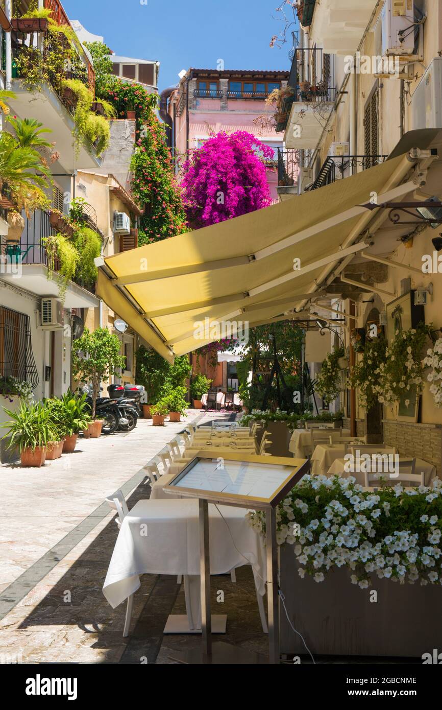 Taormina, Messina, Sicily, Italy. A charming flower-filled corner of the Old Town, typical trattoria in foreground with tables set for lunch. Stock Photo