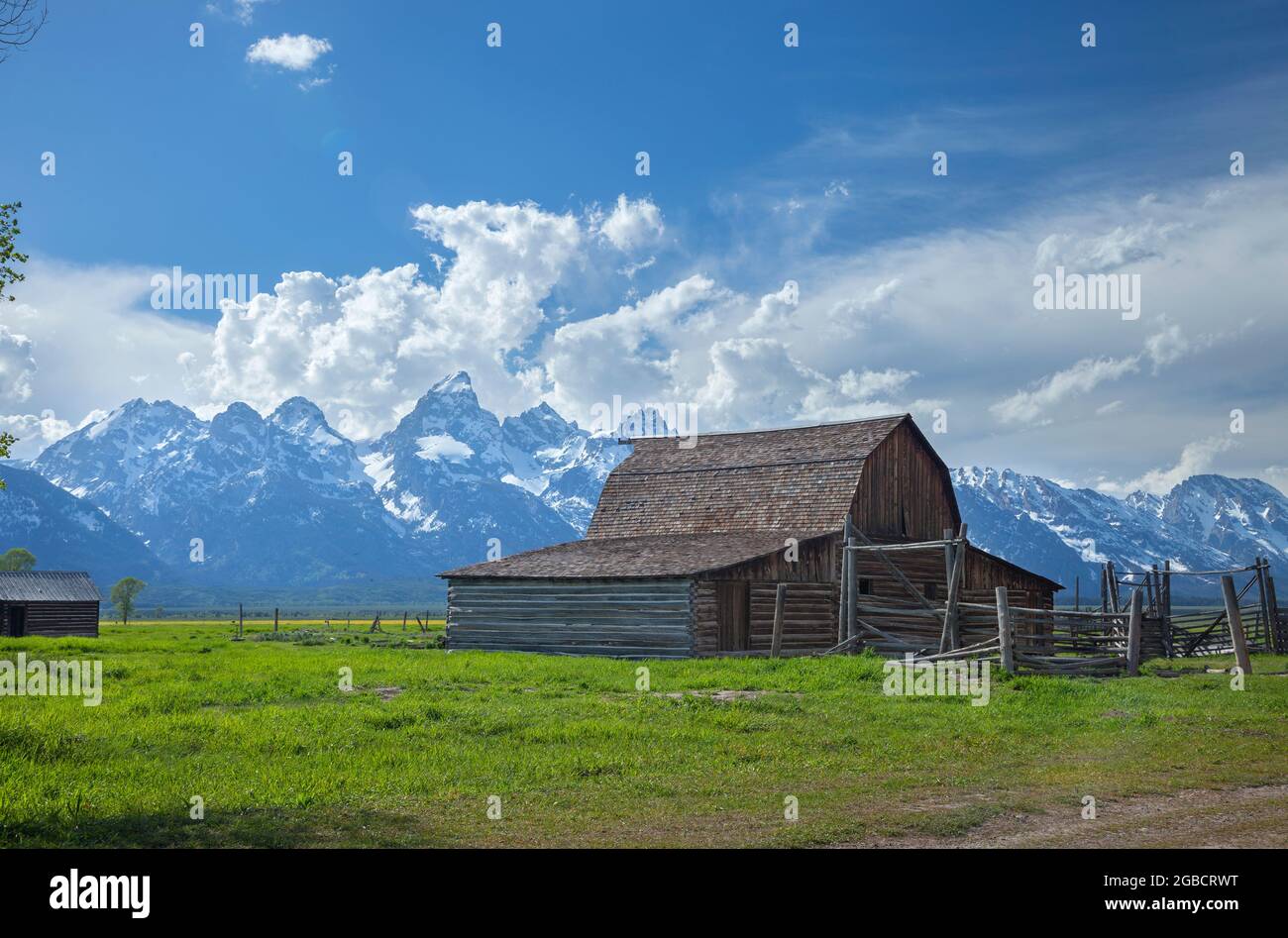 Old barn in a field under the Grand Teton mountains with dramatic clouds on a sunny afternoon Stock Photo