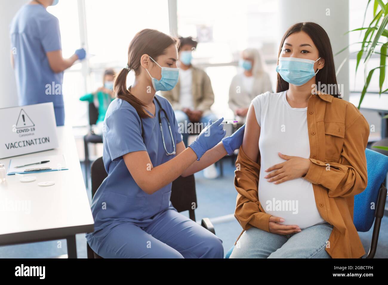 Doctor Making Coronavirus Vaccine Injection To Pregnant Asian Woman Stock Photo