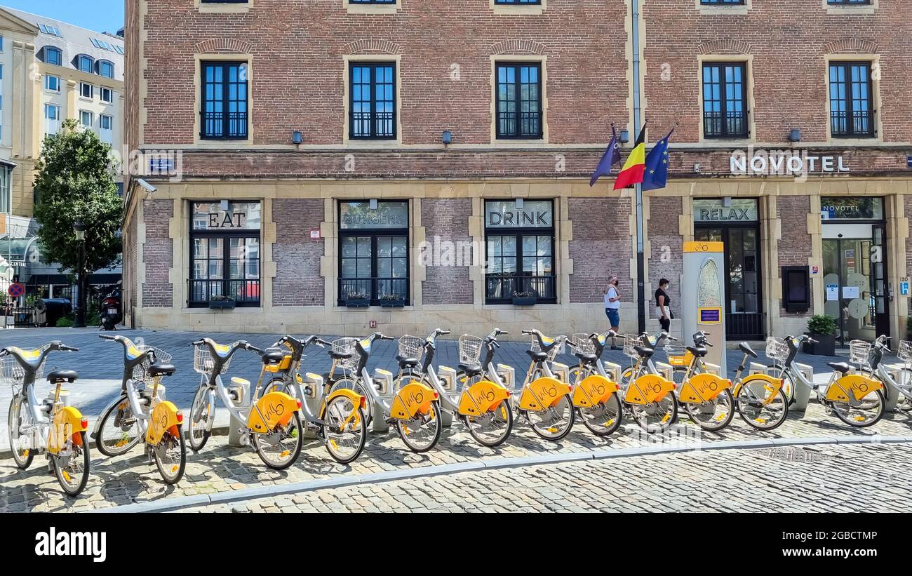 A row of city bikes for rent parked on the central square in front of the hotel Novotel on a sunny day. Stock Photo
