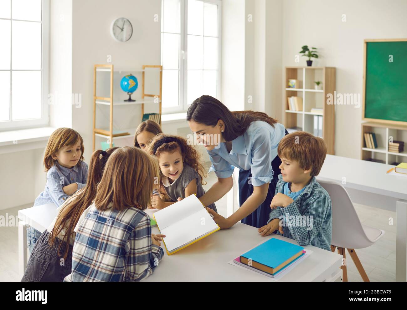 Happy young school teacher and group of elementary students reading book together Stock Photo