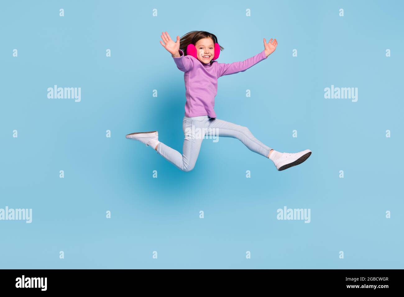Full length body size photo small girl jumping wearing fluffy headphones isolated pastel blue color background Stock Photo
