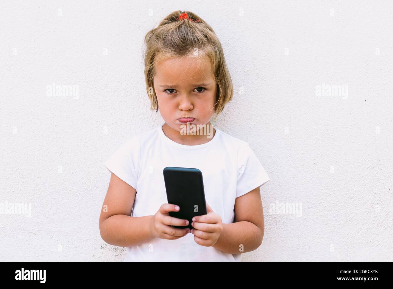 Little blond hair girl wearing white t-shirt, holding mobile phone ...