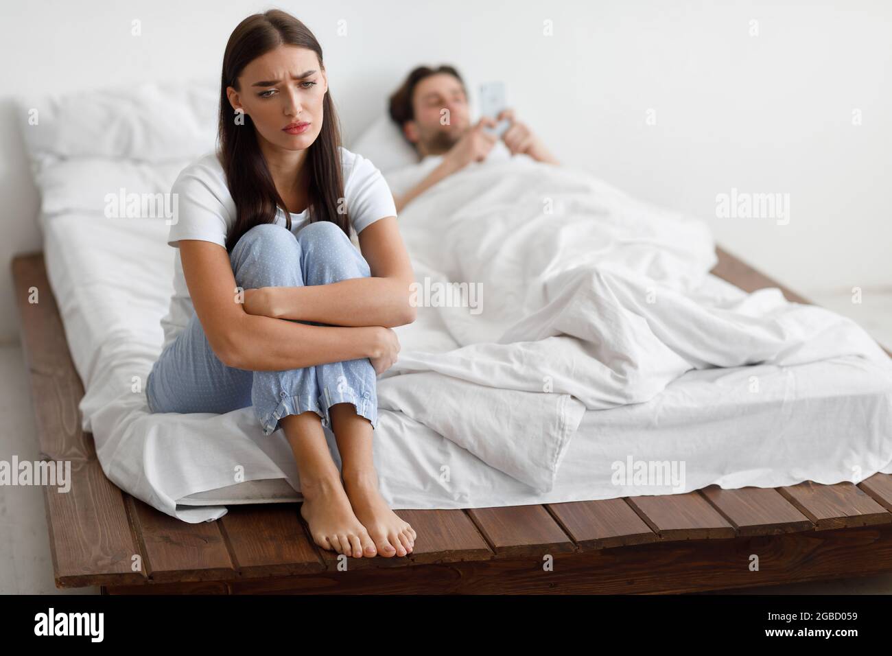 Unhappy Wife Suspecting Infidelity While Cheating Husband Texting In Bedroom Stock Photo