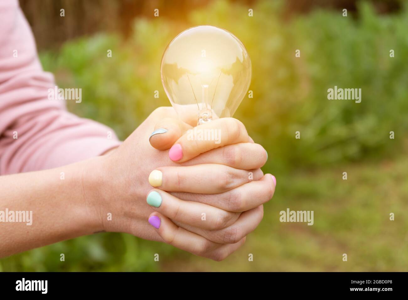 Energy and environment eco concept.Woman hands holding glowing light bulb in nature background. Stock Photo
