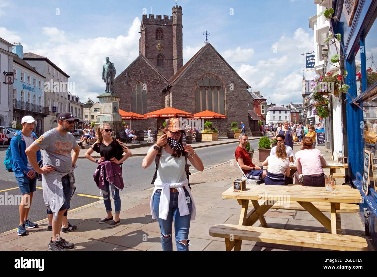 Woman puts on covid face mask outside restaurant staycation 2021 & family waiting to sit at picnic table in Brecon town centre Wales UK  KATHY DEWITT Stock Photo