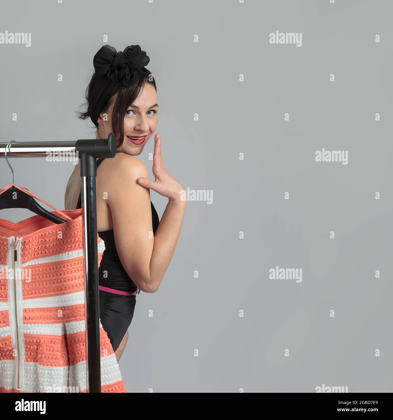 Portrait of a beautiful woman in a black bikini, standing near the hangers with clothes, thinking about what to wear. Copy space. Stock Photo