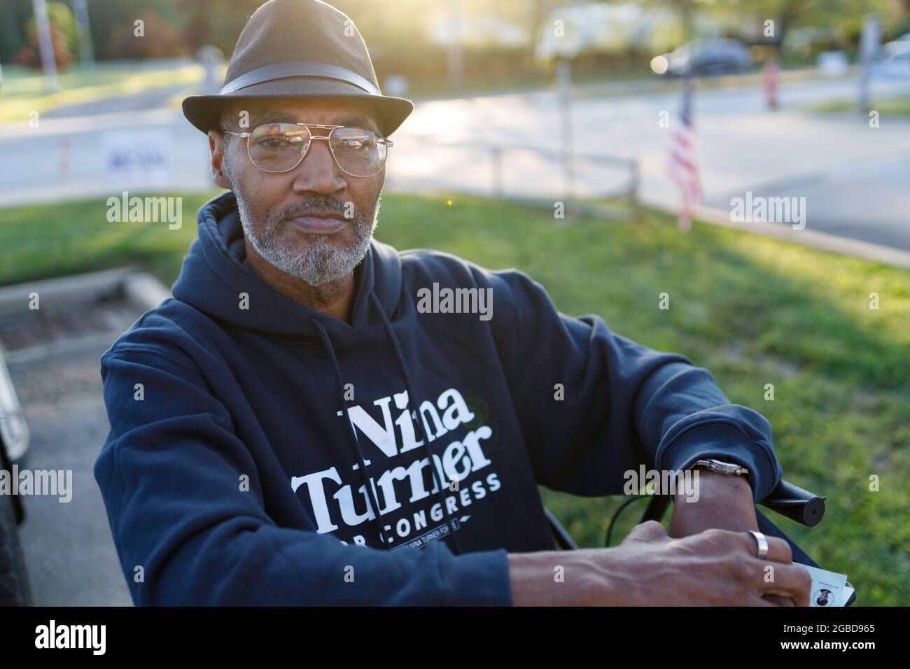 Erwin Johnson, 61, of Cleveland, Ohio sits for a portrait outside of the Warrensville Heights Recreation Center while a car with a Shontel Brown sticker drives by. Johnson came to show support for Nina Turner because, “I think she's the best candidate. She's been a state rep, She's the most qualified.” Voters came out to the polls for a special election in Ohio's 11th district. The two main leading candidates for this House of Representatives seat are two Democrats, Nina Turner, a progressive candidate, and Shontel Brown, who represents the traditional Democratic establishment. Stock Photo