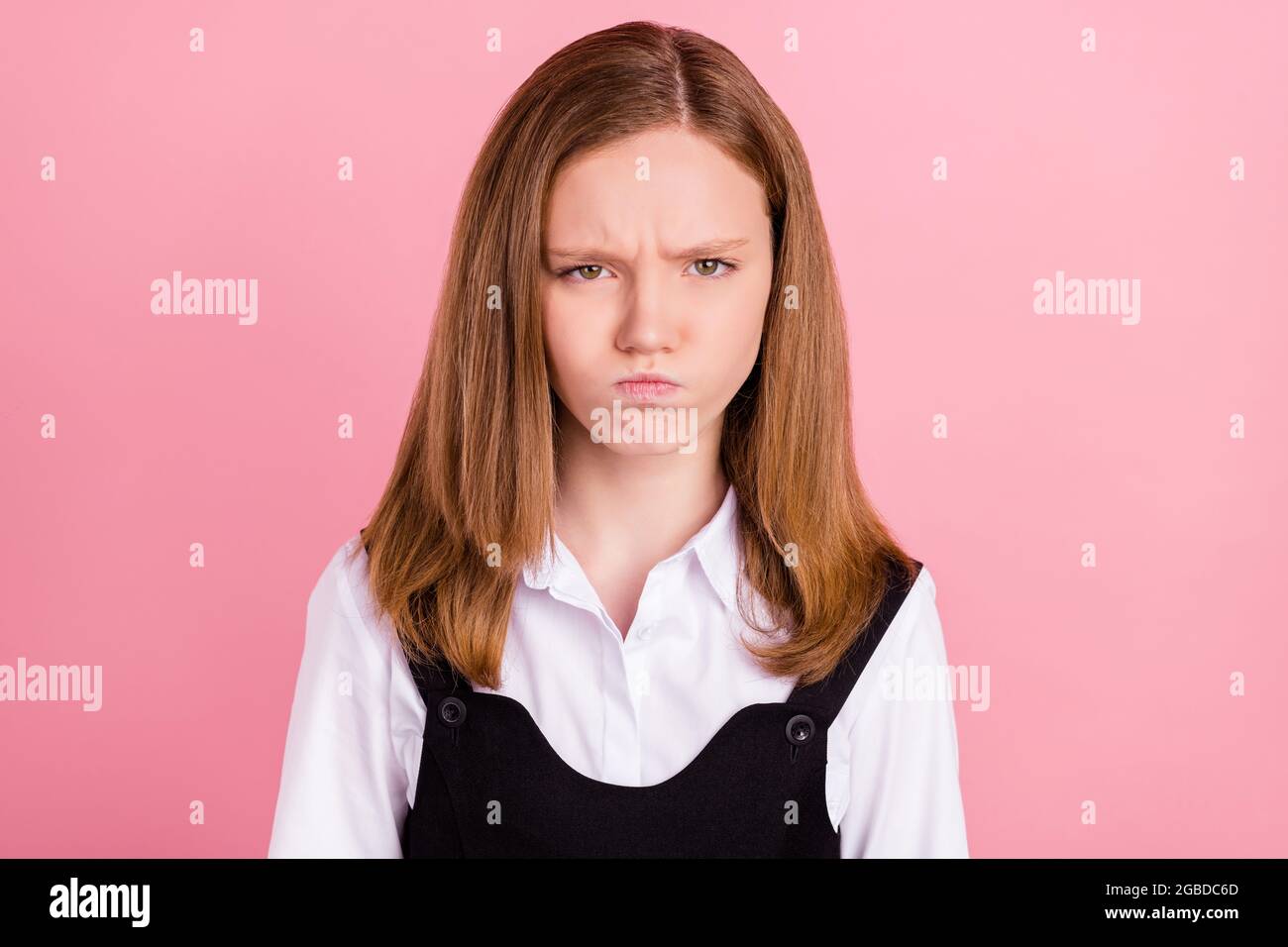 Photo of angry beautiful school girl wear black white uniform bloated cheeks isolated pink color background. Stock Photo
