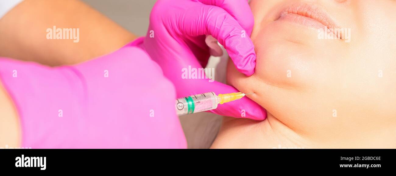 The cosmetologist makes lipolytic injection on the chin of a young woman against the double chin in a beauty salon Stock Photo