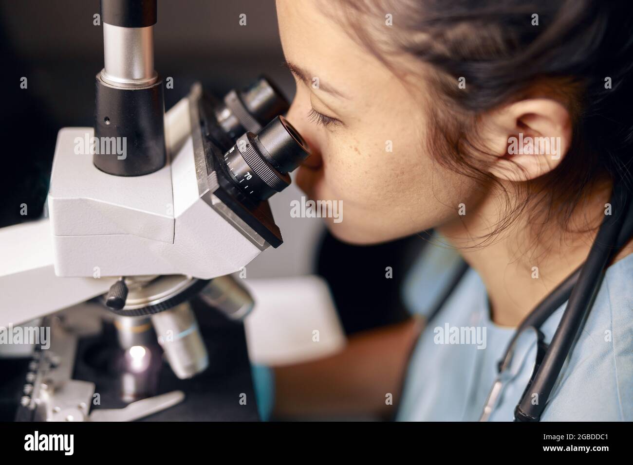 Asian lady doctor looks into contemporary microscope researching sample on slide in hospital Stock Photo
