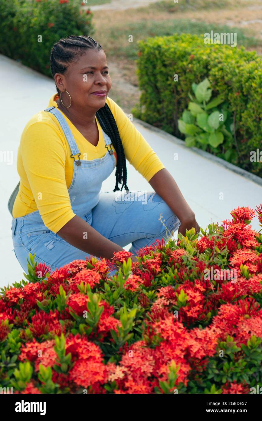 Mature Black woman posing near red flowers in the open air Stock Photo