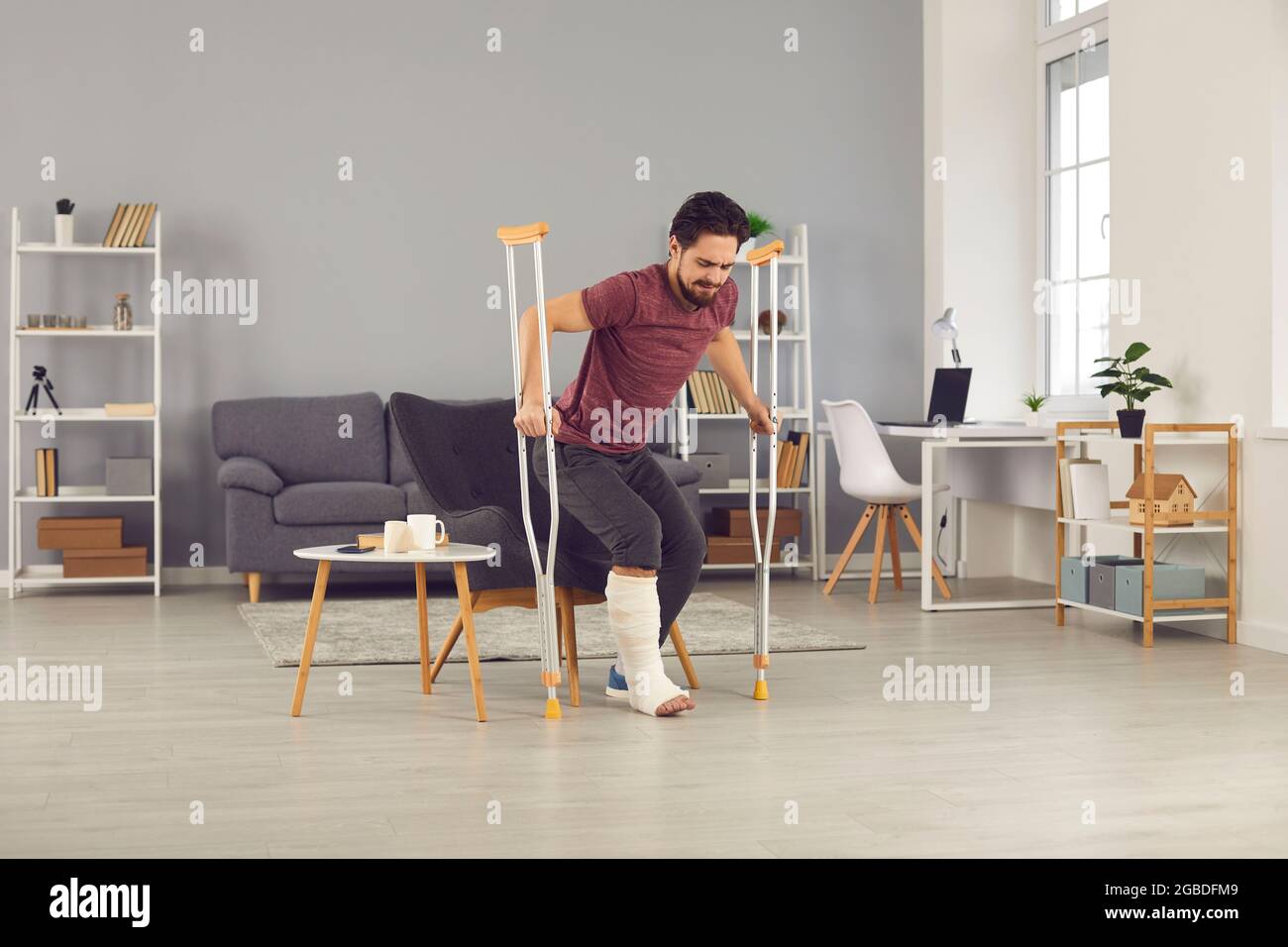 Man with broken leg trying to stand up from chair and walk with