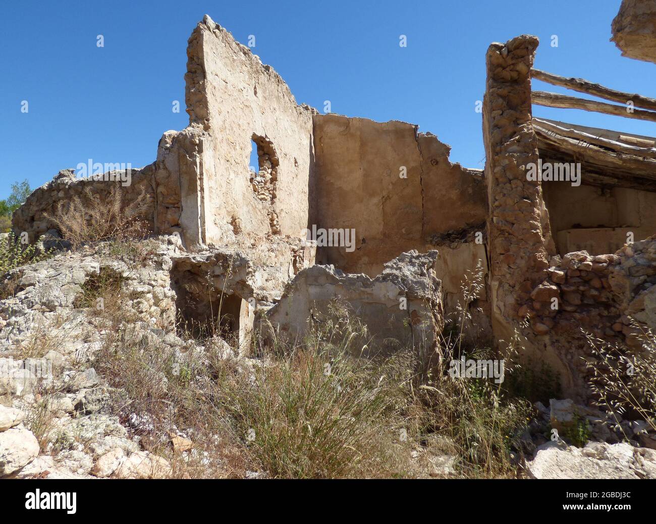 A completely dilapidated stone house in the Spanish sunshine. Nature takes over. A ruin in a very dry landscape. The sky is cloudless blue. Stock Photo