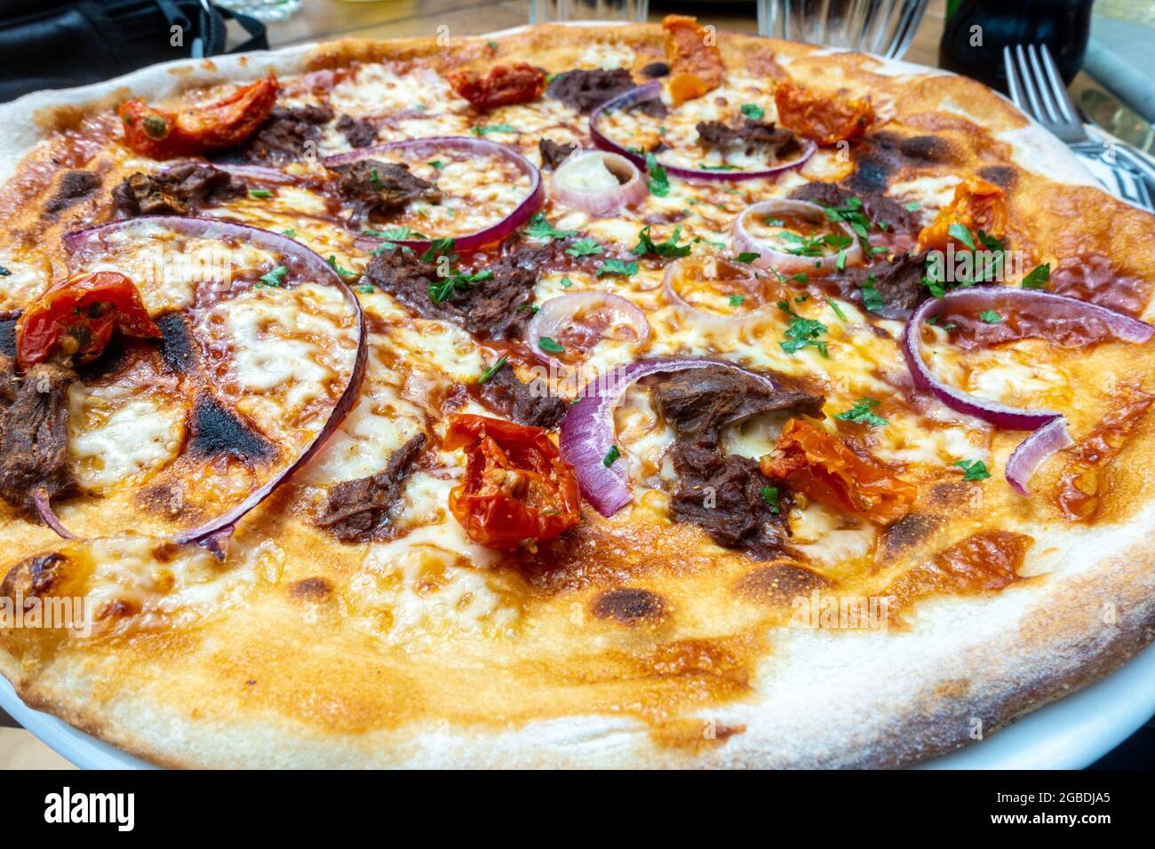 An Italian thin crust pizza with red onion, beef and cheese at a restaurant. Stock Photo