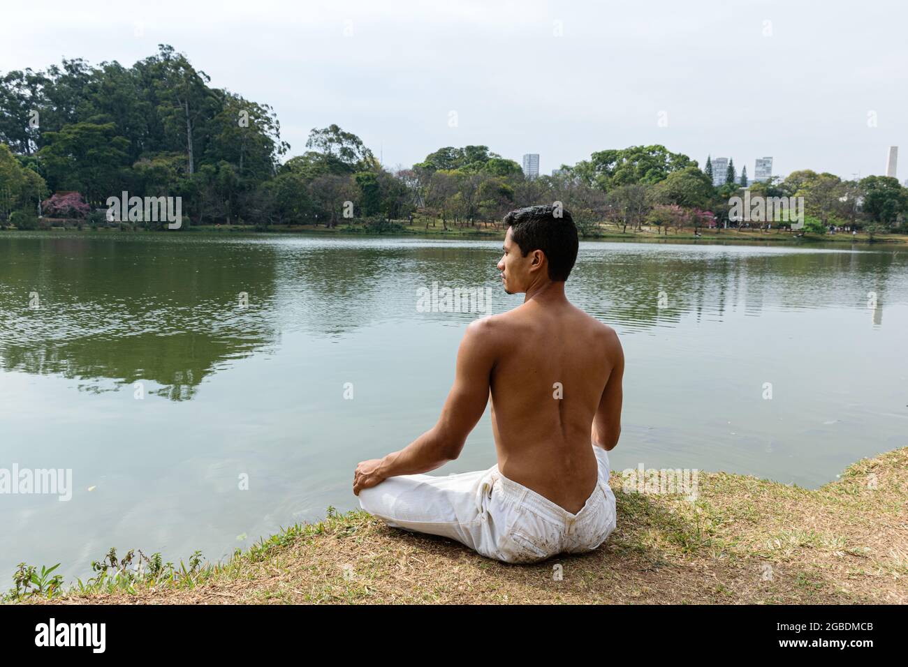 Brazilian young man sitting back to back on the edge of a lake in meditation position. Stock Photo