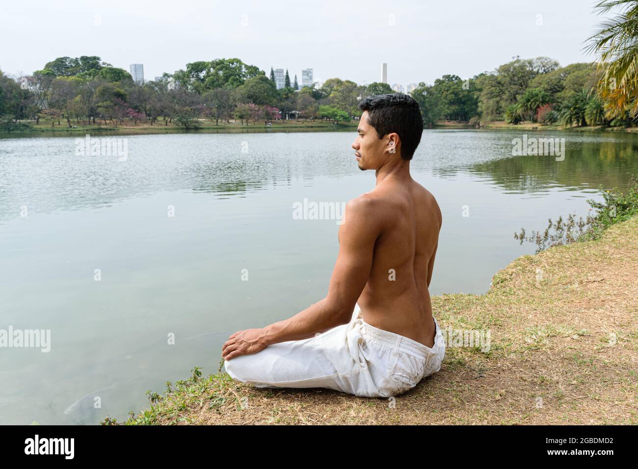 Brazilian young man sitting looking at the lake in meditation position. Stock Photo