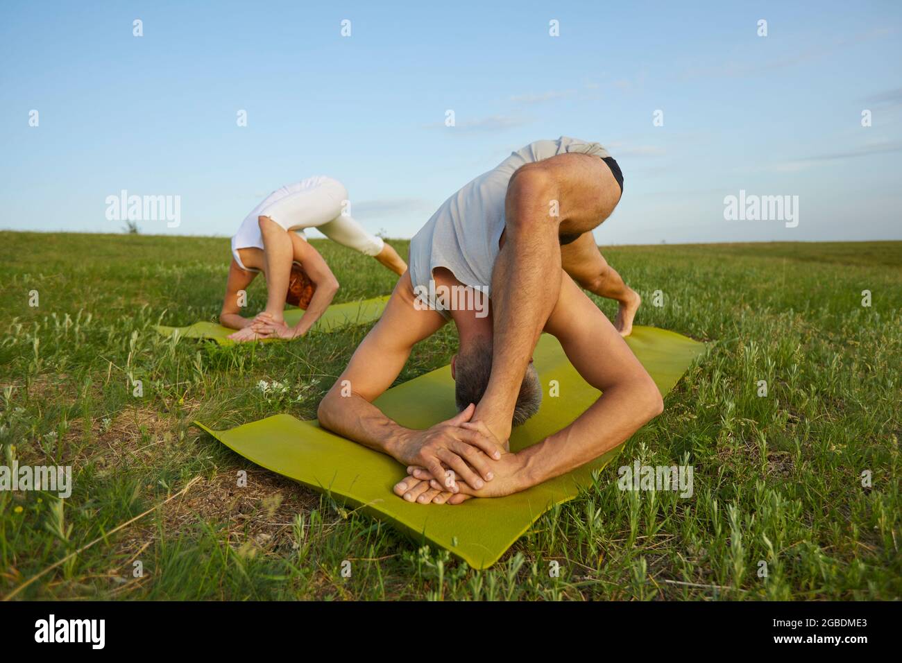Man and woman doing complicated bending exercises on green grass in summer field Stock Photo