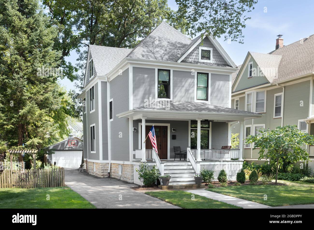 A beautifully renovated Victorian home with a grey and white siding, a covered front porch and a