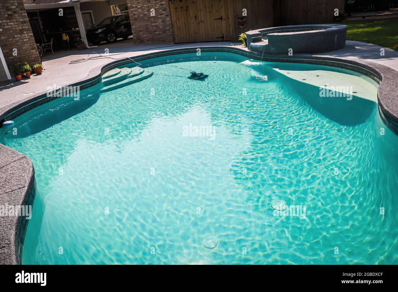 A large free form gray grey accent swimming pool with turquoise blue water in a fenced in backyard in a suburb neighborhood. Stock Photo