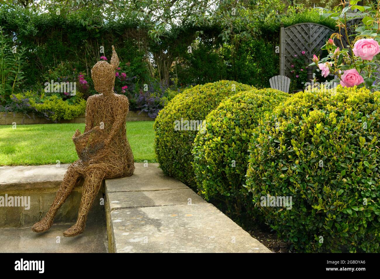 Sculpture art (ornamental feature) in beautiful colourful landscaped garden (flowering plants & shrubs, roses, box balls, lawn) - Yorkshire England UK Stock Photo