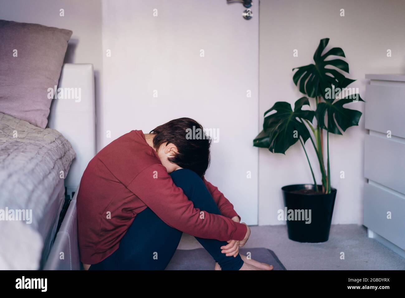Depressed and sad woman huging her knee and sitting on the floor in the bedroom. Troubled with domestic violence, unwilling pregnancy, abortion Stock Photo