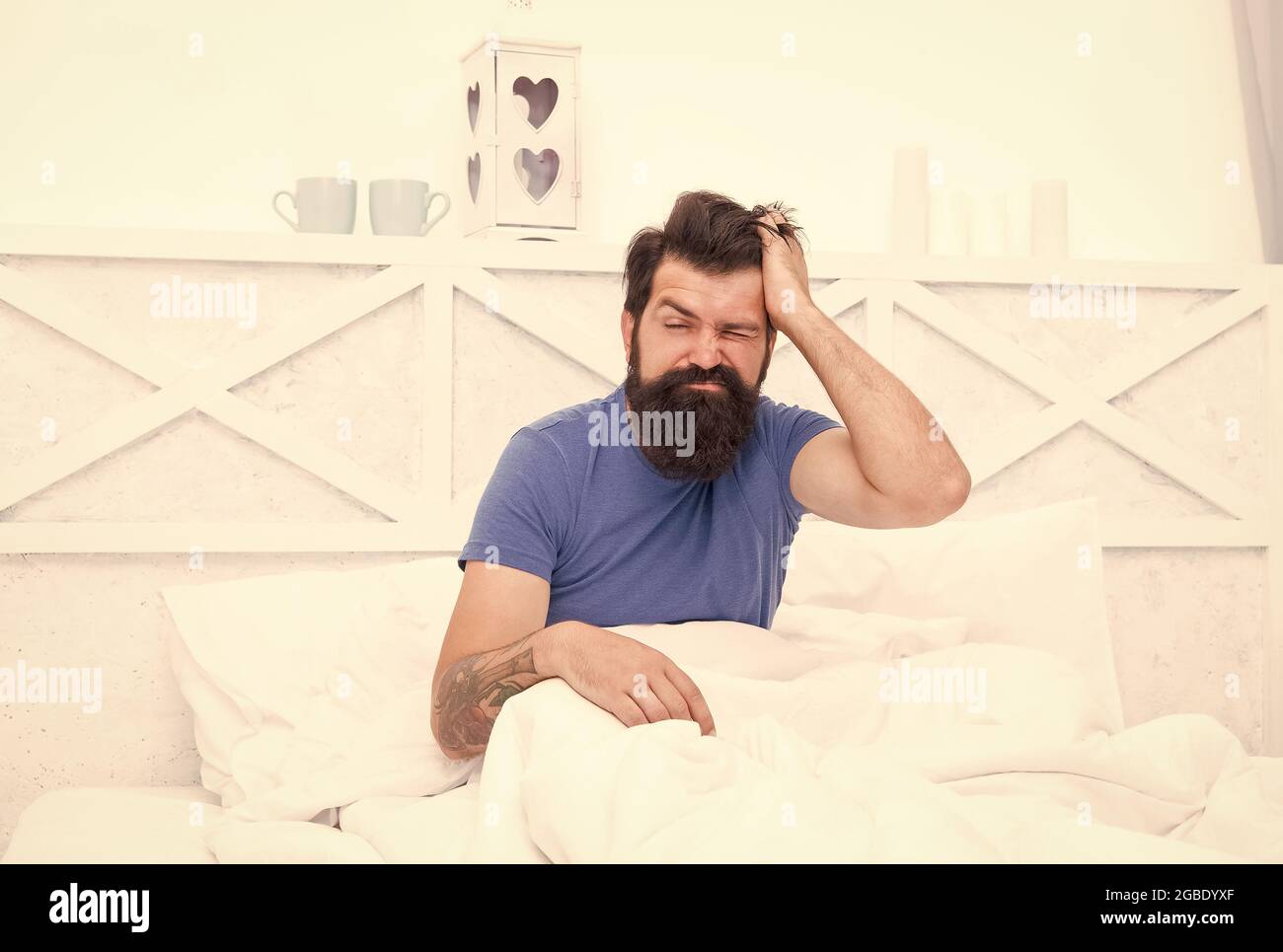 morning migraine. tired bearded man in bed. early wake up at morning. bachelor has hangover. guy at bedroom. lazy sunday. bed time routine. brutal Stock Photo