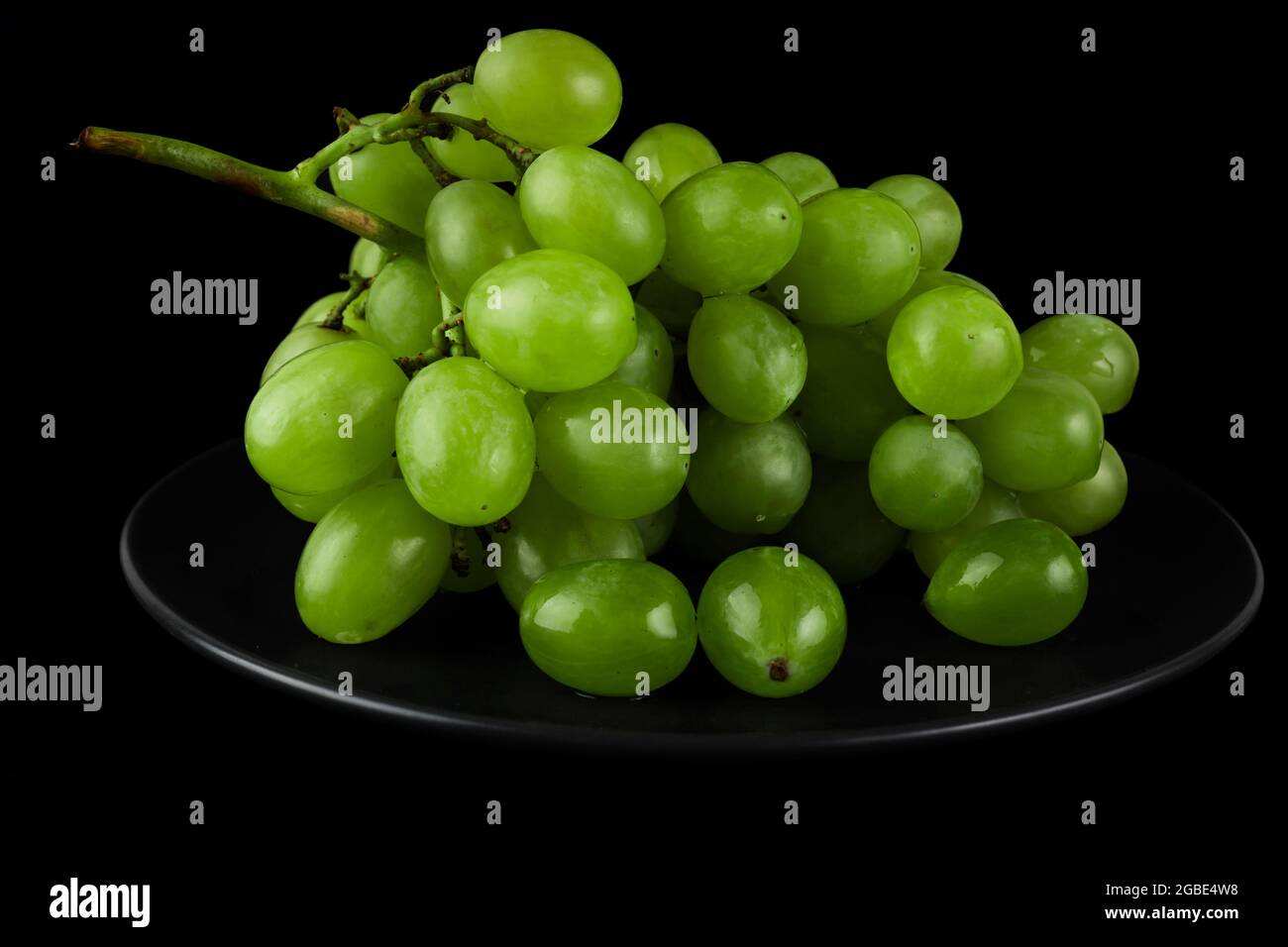 A bunch of table grapes, white pouring, on a black plate, on a black background Stock Photo