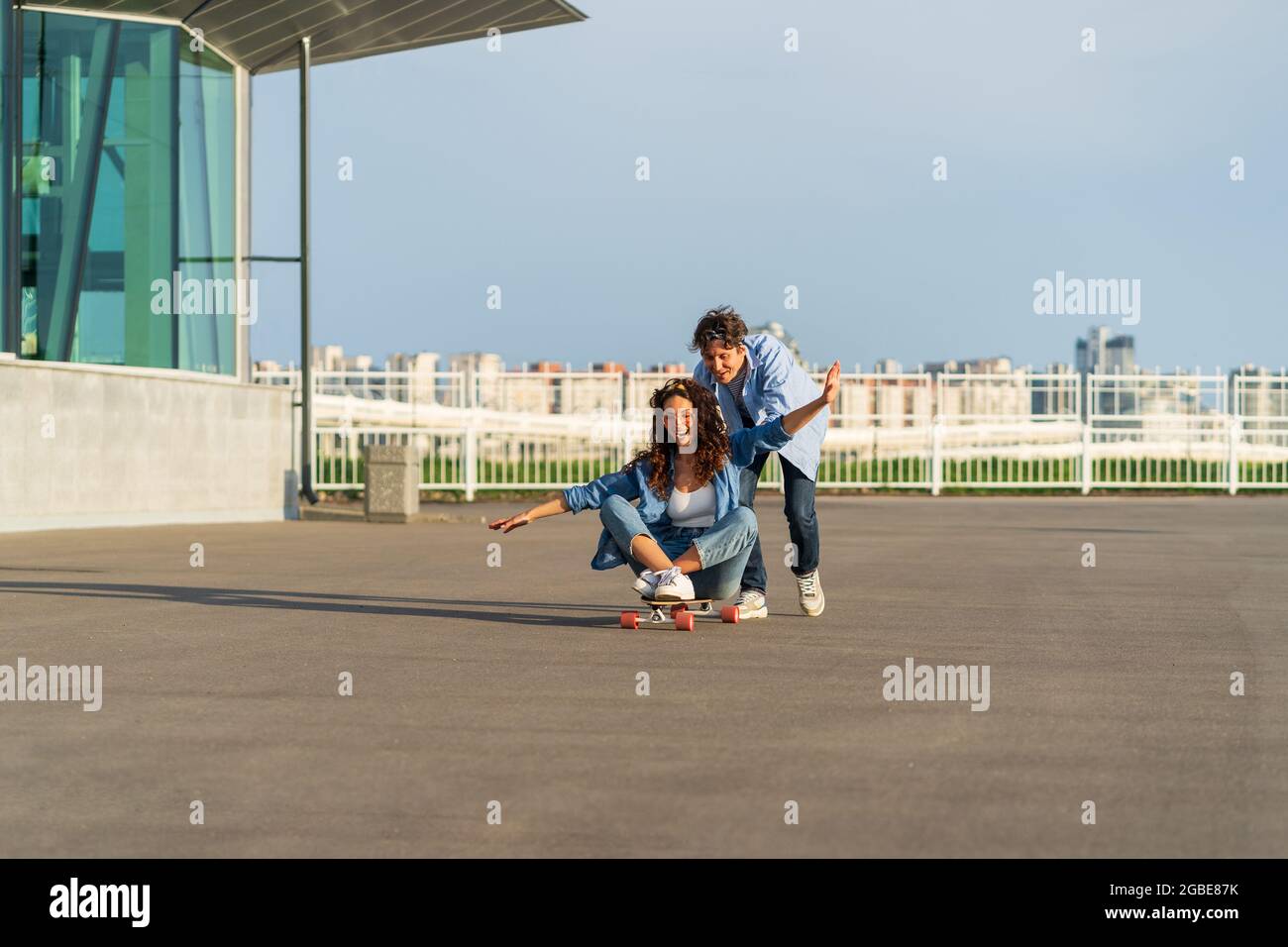 Young couple enjoy skateboarding together on street. Hipster man push back of woman sit on longboard Stock Photo