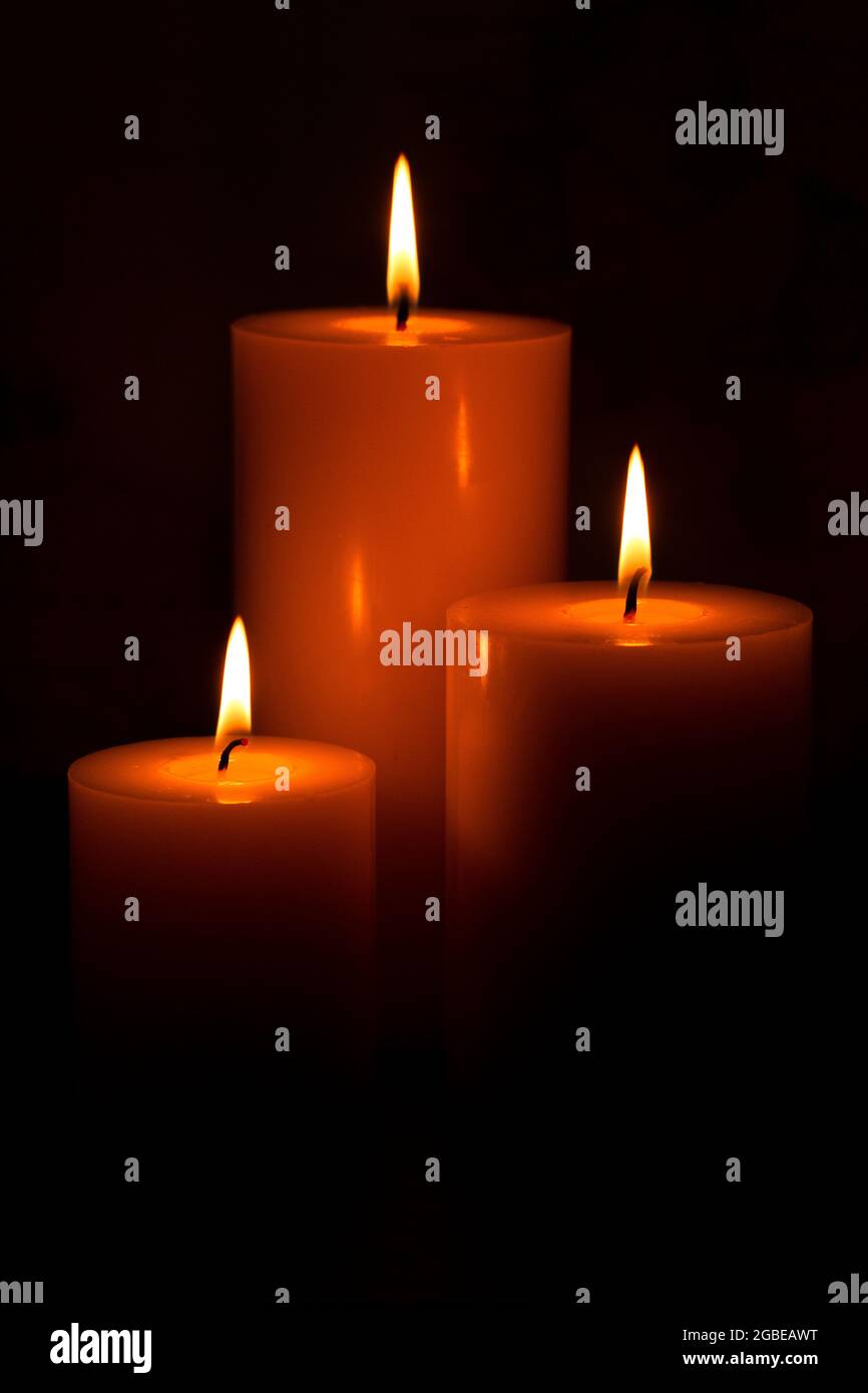 Three Pillar Candles Lit in a Dark Room Stock Photo