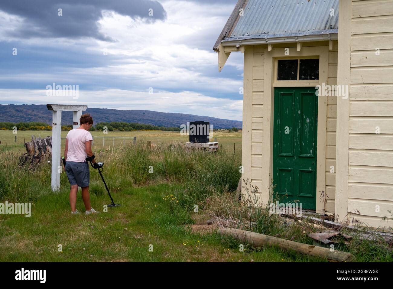 A women looks for old coins using a metal detector around an old deserted building Stock Photo