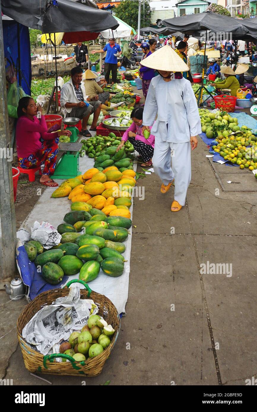 A woman wearing white pants and jacket and traditional conical hat shops at a busy outdoor market in Can Tho, Vietnam, Mekong Delta. March 9, 2018. Stock Photo