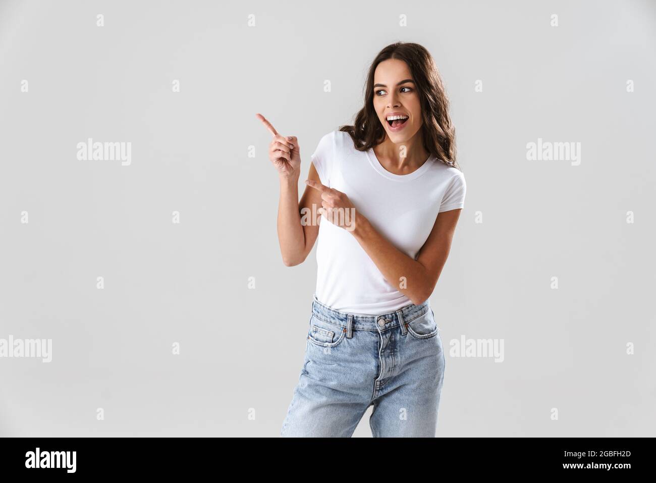 Excited beautiful girl smiling and pointing fingers aside isolated over ...