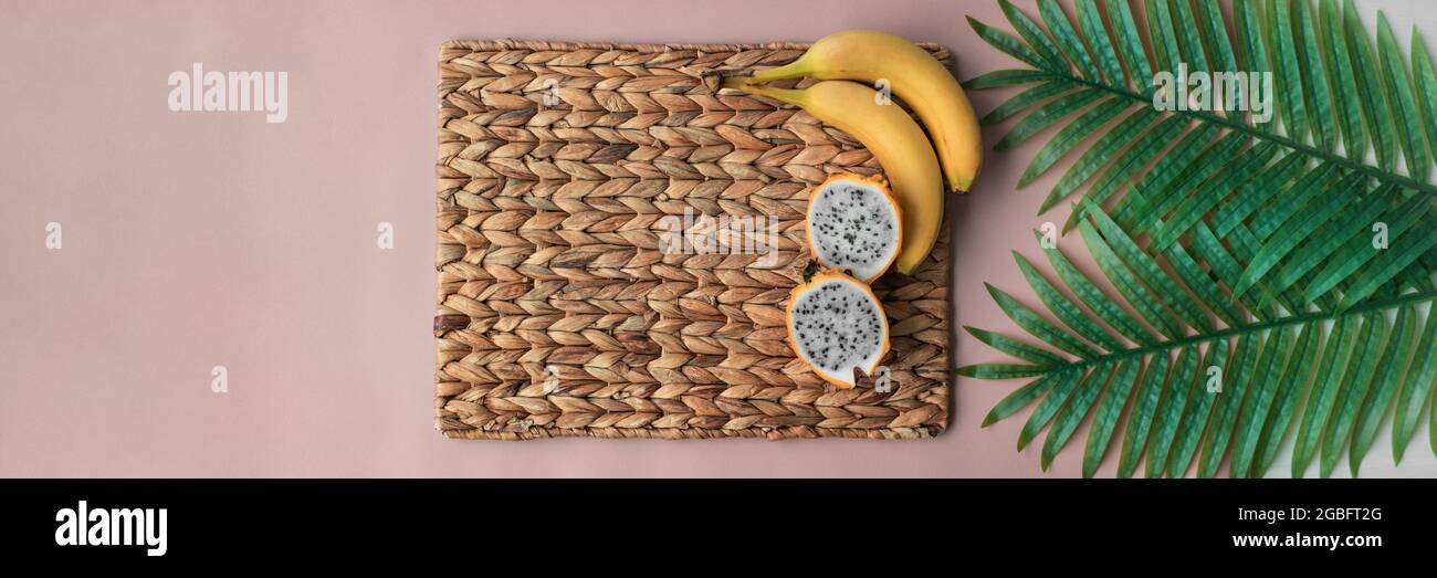 Pitaya and bananas tropical fruits top view of breakfast morning table background. Banner on pink and straw placemat Stock Photo