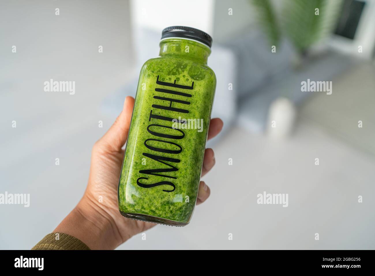 Green smoothie healthy drink bottle woman taking first person view food selfie holding juice at home for detox diet. View of hand Stock Photo