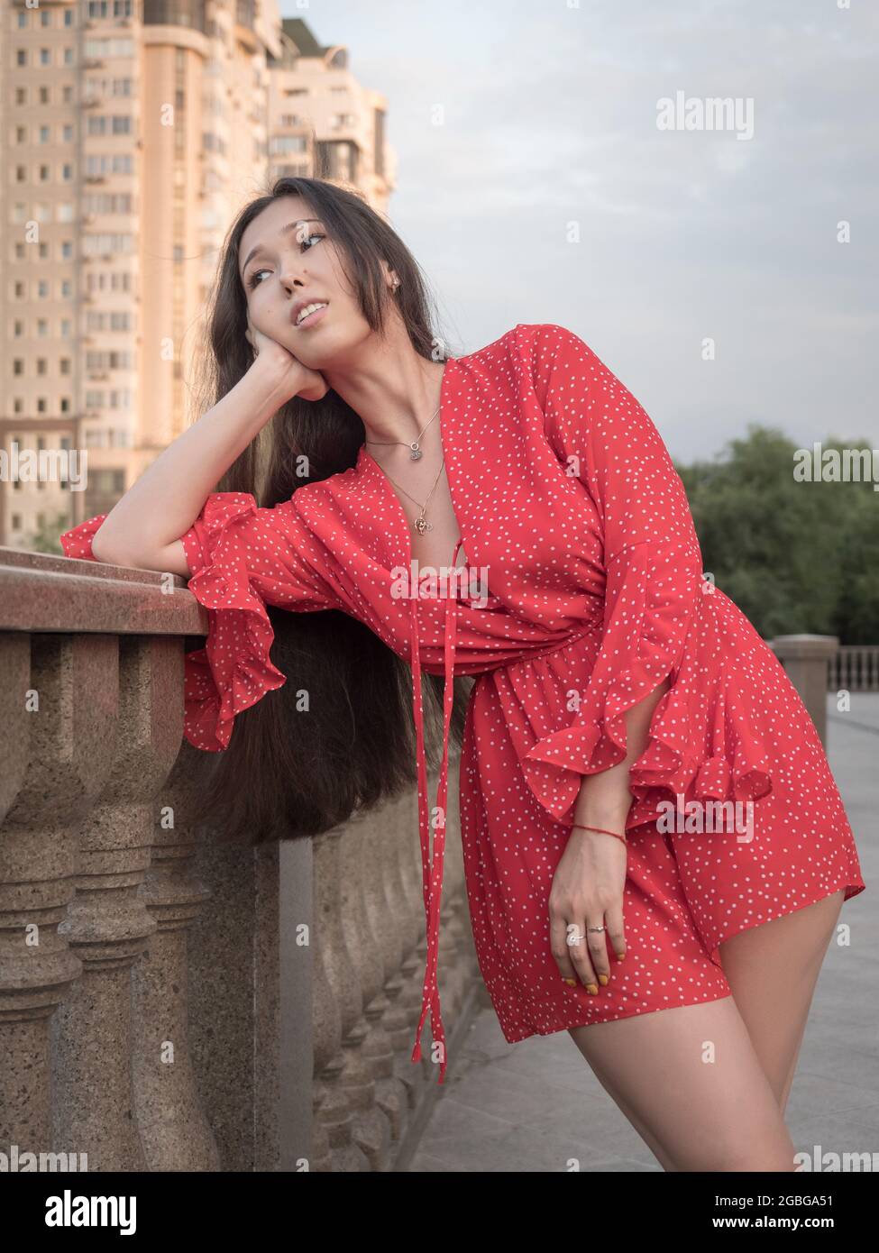 Attractive smiling Asian girl in red dress posing in the city near the ...